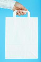 White Paper bag at arm's length isolated on a blue background. Layout of the packaging template with space for copying, advertising. photo