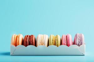 Macaroni cookies of different colors in a white box on a blue background. photo