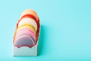 Macaroni cookies of different colors in a white box on a blue background. photo