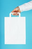 Paper bag at arm's length, white craft bag for takeaway isolated on blue background. Packaging template layout with space for copying, advertising. photo