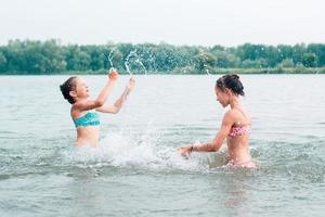 Two cheerful girls play with splashes in the river. Local tourism. Summer vacation photo