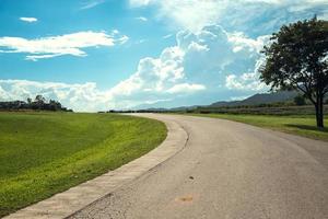 Panorama scene of curve asphalt road in the countryside on sunny spring day. Route in beautiful nature landscape with green grass, cloud and sun. Copy space for traveling advertisement. photo