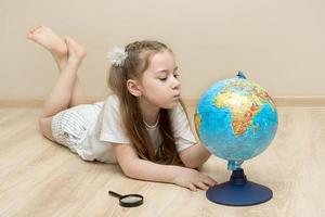 little girl lies on the floor and carefully examines the globe photo