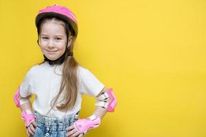 little cute girl in protection for roller skating or cycling stands on a yellow background with her hands on her belt and smiles, the concept of protect your child photo