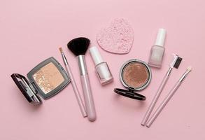 Cosmetic brushes, powder, blush, nail polish on pink background. photo