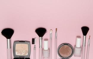 Cosmetic brushes, powder, blush, nail polish on pink background with place for text above. photo