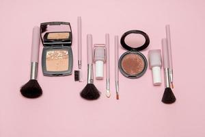Cosmetic brushes, powder, blush, nail polish on pink background lie in a row photo