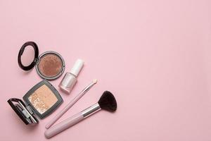 powder, makeup brushes, nail polish, blush on a pink background with space for text photo