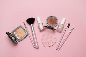 Cosmetic brushes, powder, blush, nail polish on pink background photo