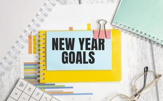 new year goals words and yellow notebook with charts and glasses photo