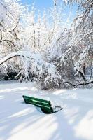 banco verde en un jardín urbano cubierto de nieve en invierno foto
