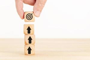 Business achievement goal and objective target concept. Hand holding a cube with dartboard and arrows on stacked blocks. Copy space photo