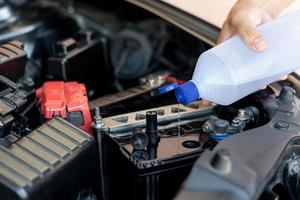 un hombre agrega agua para destilar el mantenimiento de la batería del automóvil y las inspecciones para prolongar la vida útil del automóvil foto