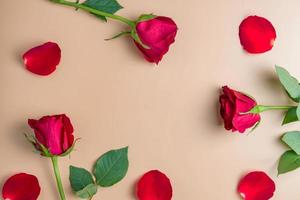Border frame made of red roses and flower petals on beige background. Flat lay, top view. Frame of flowers. photo