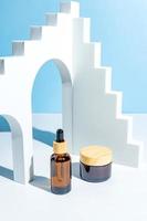 Moisturizer cream jar, serum in amber glass bottle on blue background. trendy podiums for cosmetics presentation. Set for skin and body care beauty products photo