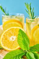 Glass of water with orange, mint and rosemary on blue background photo