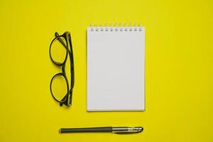 Minimal composition with blank blaktoth, glasses and pen on yellow table, flat photo