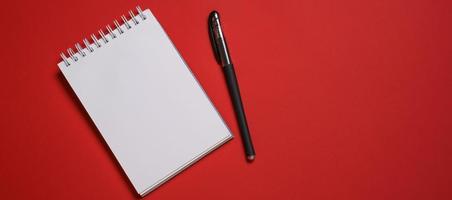 Open notebook on a spring and a black ballpoint pen on a red background copy photo