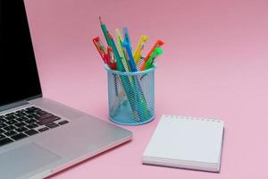 Laptop pens and colored pencils in blue stand and white stickers on pink photo