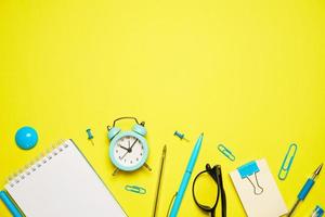 Notebook for writing pen and alarm clock with glasses on yellow background top photo