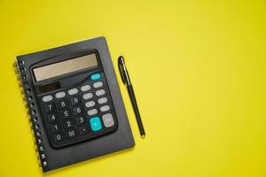 Notepad on spring black calculator and ballpoint pen on yellow background photo
