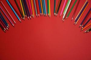 Colored wooden pencils scattered on red background, education concept. photo