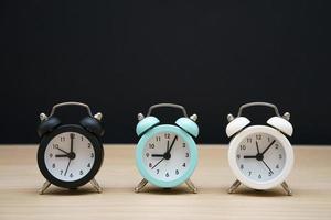 Three small alarm clocks black blue and white show nine o'clock, stand photo