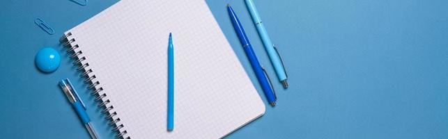 Notebook and pen on a blue background. Top view with copy space. Stationery photo