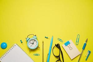 Notebook for writing pen and alarm clock with glasses on yellow background top photo