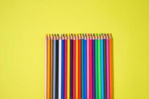 Assortment of colored pencils in various iridescent colors on a yellow photo