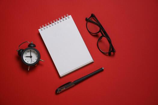 Alarm clock glasses notepad pen on table, red background, text space, selective photo