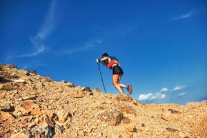 Young woman uphill on rocky slope pushes with poles photo