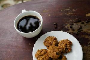 taza de café negro con galletas en el suelo de madera, café negro por la mañana para beber con galletas. foto