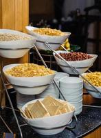 A vertical shot of a buffet table full of bowls with cornflakes, peanuts and cereal for breakfast photo