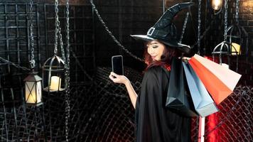 Portrait beautiful woman wearing witch costume holding shopping bag and mobile. Emotion smile photo