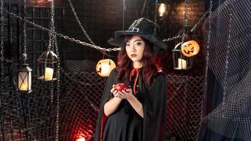 feliz halloween, joven asiática disfrazada de bruja con sombrero de bruja sosteniendo manzana en el tema de halloween. foto