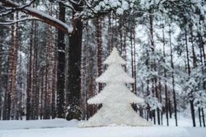 tiro horizontal de árbol de año nuevo blanco artificial se encuentra en el bosque de invierno contra árboles naturales. foto al aire libre del árbol blanco de navidad en la hermosa naturaleza