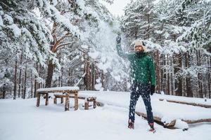 Outdoor shot of handsome bearded male dressed in warm clothes, has fun as throws snow in air, spends holidays in winter forest, expresses positiveness. Recreation and weather concept photo