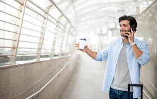 The man using the smartphone while the other hand holding a cup of coffee and pulling the luggage at the airport. photo