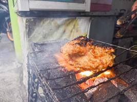 pechuga de pollo envuelta en harina crujiente con deliciosos condimentos picantes a la parrilla sobre carbón ardiendo sin llama. un pollo asado típico de indonesia foto