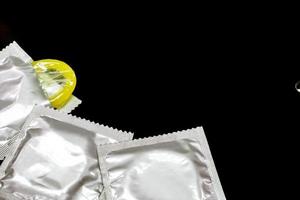 Condom in silver packages and one opened crops and do copy space isolate on  black background. photo