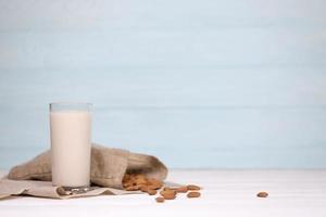 Glass of almond milk with almond nuts on canvas fabric on white wooden table. Dairy alternative milk for detox, healthy eating and diets photo