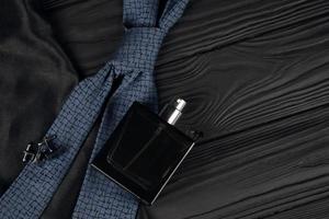 A bottle of mens cologne and cufflinks with blue tie lie on a black luxury fabric background on a wooden table. Mens accessories photo