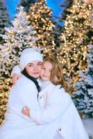 Asian mother and her Caucasian daughter by the christmas tree outdoors. Love, family, diversity, holidays concept photo