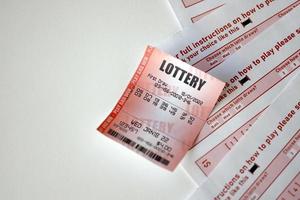 Red lottery ticket lies on pink gambling sheets with numbers for marking to play lottery. Lottery playing concept or gambling addiction. Close up photo