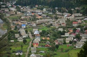 A beautiful view of the village of Mezhgorye, Carpathian region. A lot of residential buildings surrounded by high forest mountains and long river photo