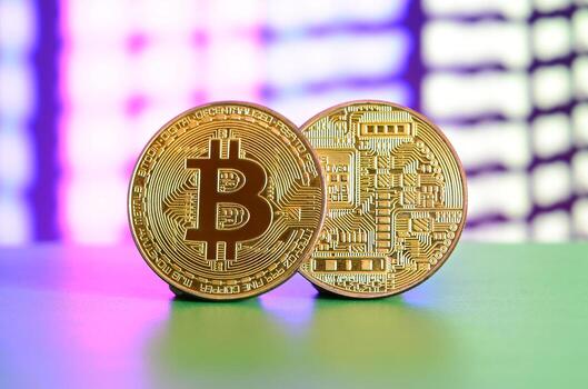 Two gold bitcoins lie on the green surface on the background of the display, which shows the process of mining the crypto currency photo
