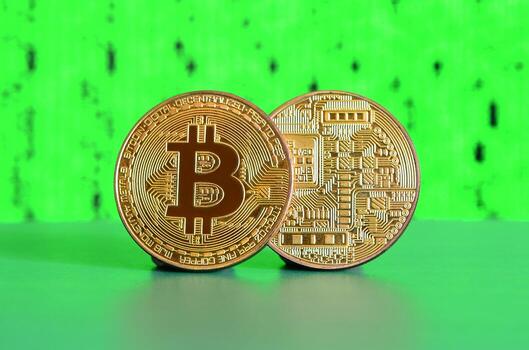 Two gold bitcoins lie on the green surface on the background of the display, which shows the process of mining the crypto currency photo