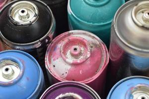 Large number of used colorful spray cans of aerosol paint lying on the treated wooden surface in the artist's graffiti workshop close up. Dirty and stained cans for art photo
