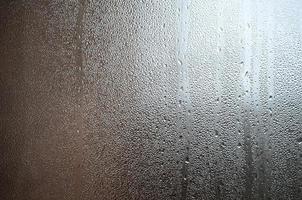 A photo of the glass surface of the window, covered with a multitude of droplets of various sizes. Background texture of a dense layer of condensate on glass